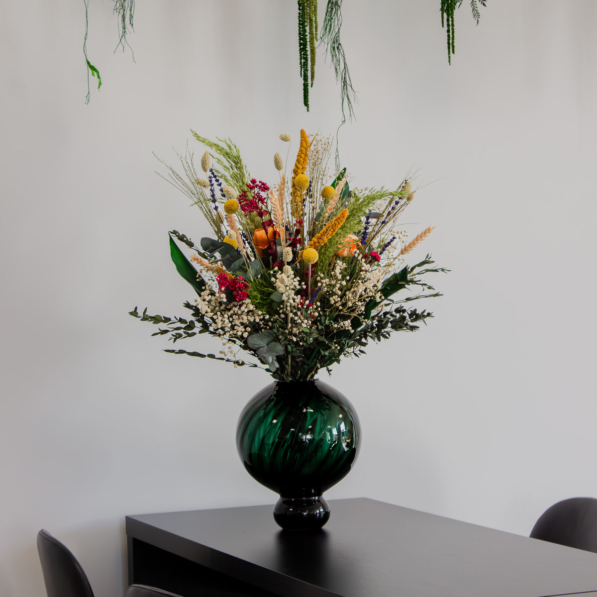 Sommerlig, naturlig bukket med langtidsholdbare blomster står i en grøn, buet vase på et bord.