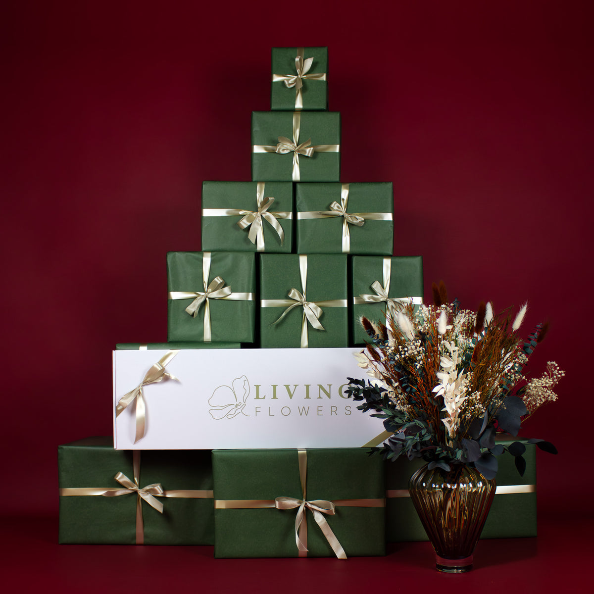Foran en pyramide af grønne gaver, hvor der også ligger en hvid Living Flowers-æske, står en glasvase med en julebuket.