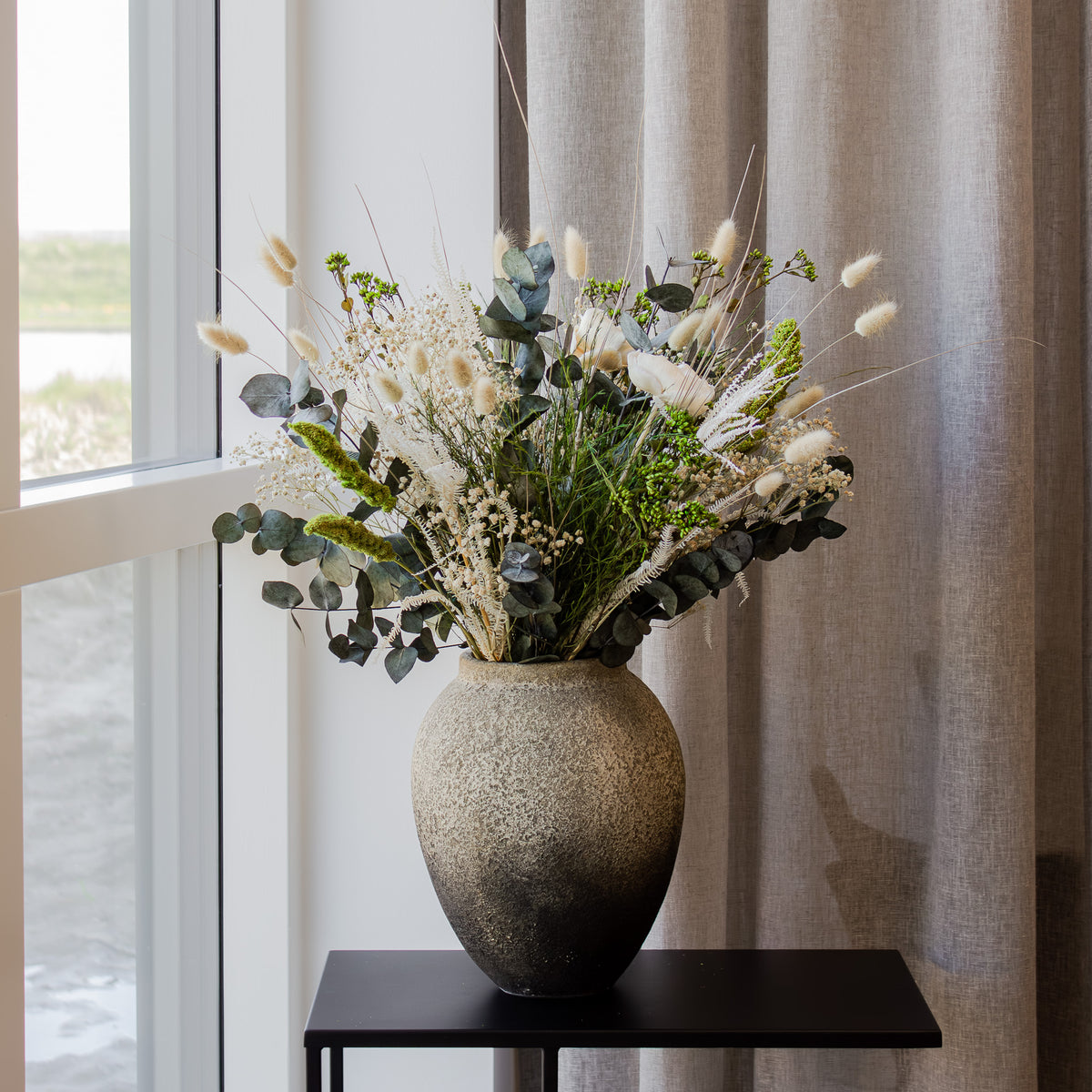 En fyldig grøn-hvid buket står i en terracottavase.