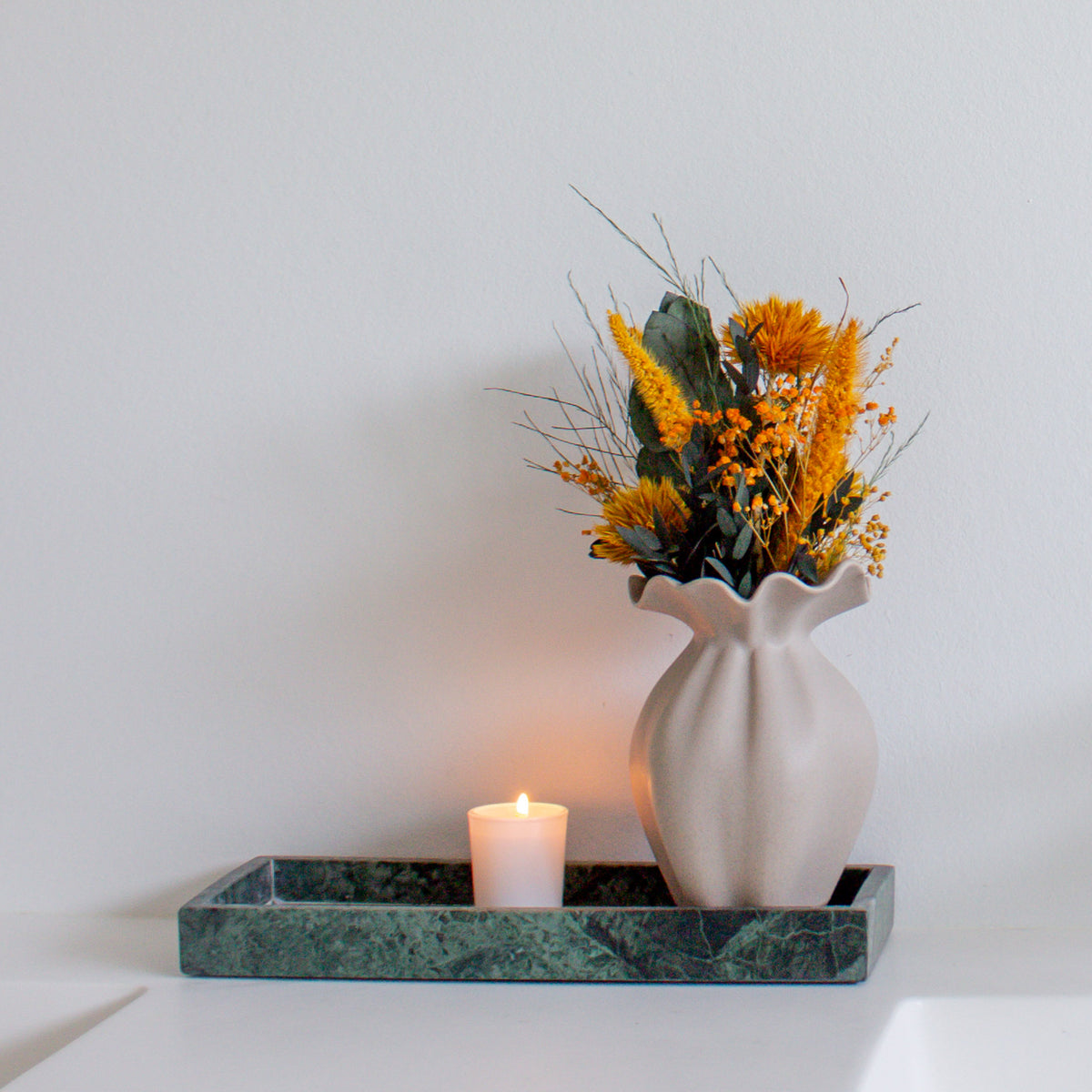 På et fad står en lille vase med en mini-buket i kraftige orange nuancer.