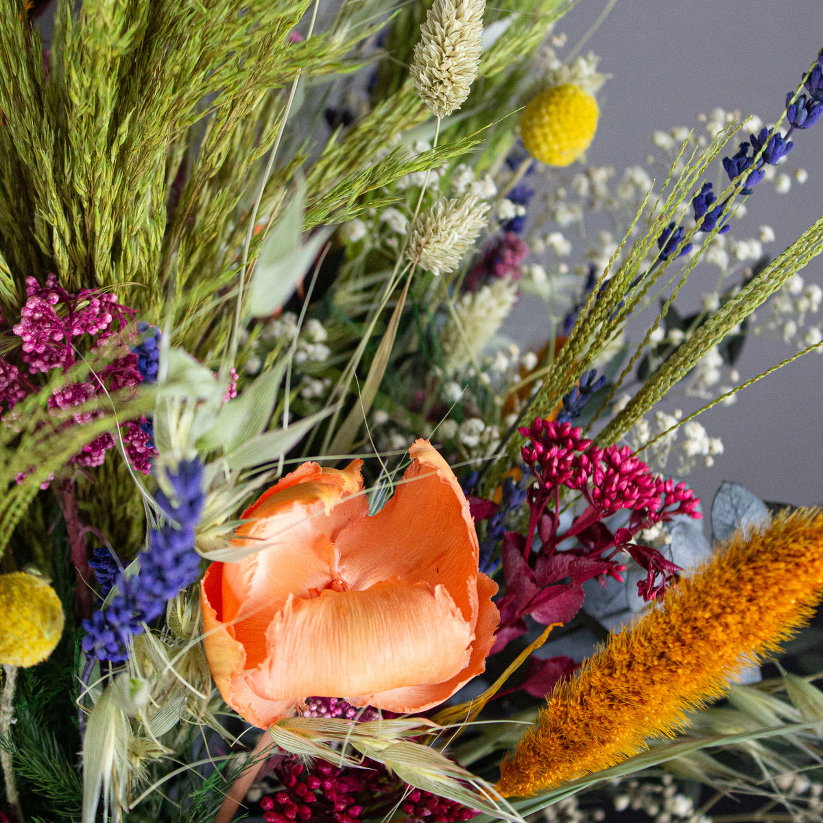 Nærbillede af en bukket med langtidsholdbare blomster i stærke farver, herunder orange, gul, lilla og grøn.