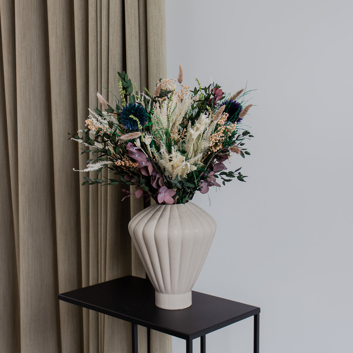 På et sidebord står en blomsterbuket i sarte farver med lilla accenter.